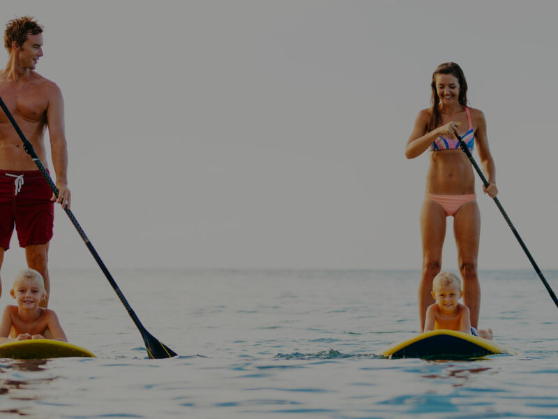 Famille en stand up paddle : deux adultes debout qui pagaient, deux enfants allongés sur leurs propres planches.